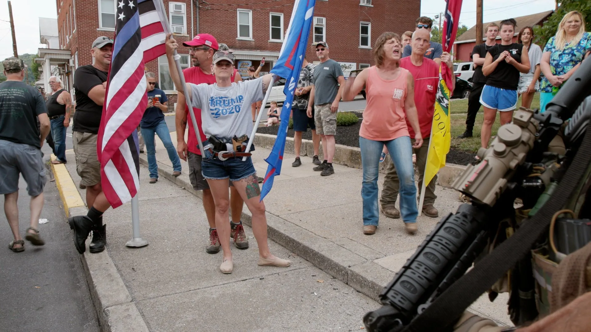 Supporters with flags and Trump signs gather at a rally in a small town